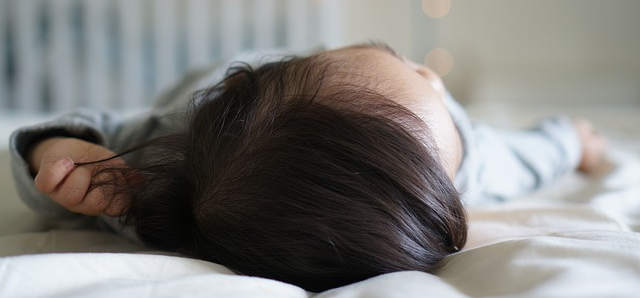 Ein Kind liegt im Babybett und schläft. Man sieht nur die schwarzen Haare und die kleine Nase des Babys.