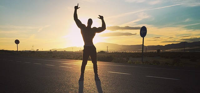 Ein Bodybuilder im Sonnenuntergang. Man sieht nur seine Konturen, da die Sonne alles weitere verdeckt.