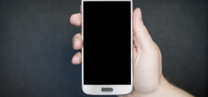 Eine Männerhand hält ein Smartphone in der Hand. Es ist ausgeschaltet. Der Bildschirm ist schwarz..