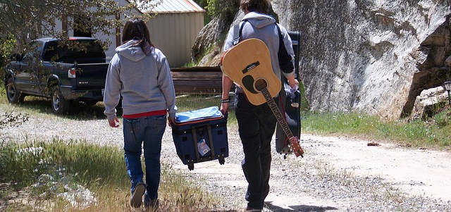 Zwei Meschen Tragen gemeinsam eine Kühlbox. Außerdem hat die linke Person eine Gitarre um sich geschnallt.