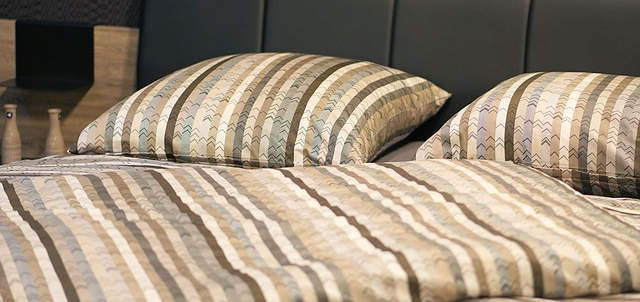 Ein Bett auf dem Bettwäsche liegt. Sie ist klassische in mehreren Farben gehalten.