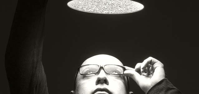 Ein Mann mit Brille und einer Glatze schaut in eine über ihm stehende Lampe.